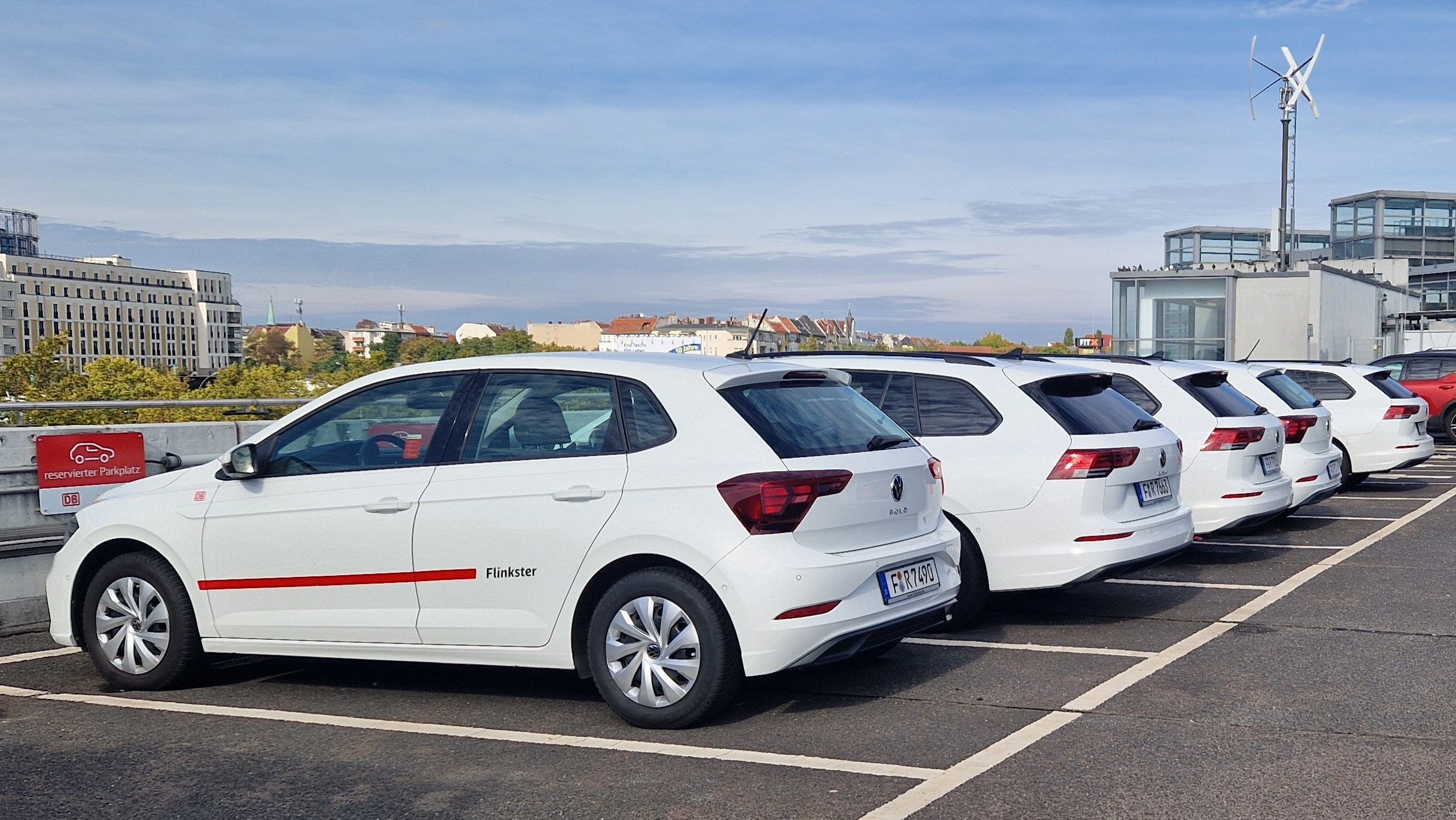 Flinkster-Carsharing-Fahrzeuge auf reservierten Parkplätzen, bereit zur Nutzung, mit städtischer Skyline im Hintergrund.