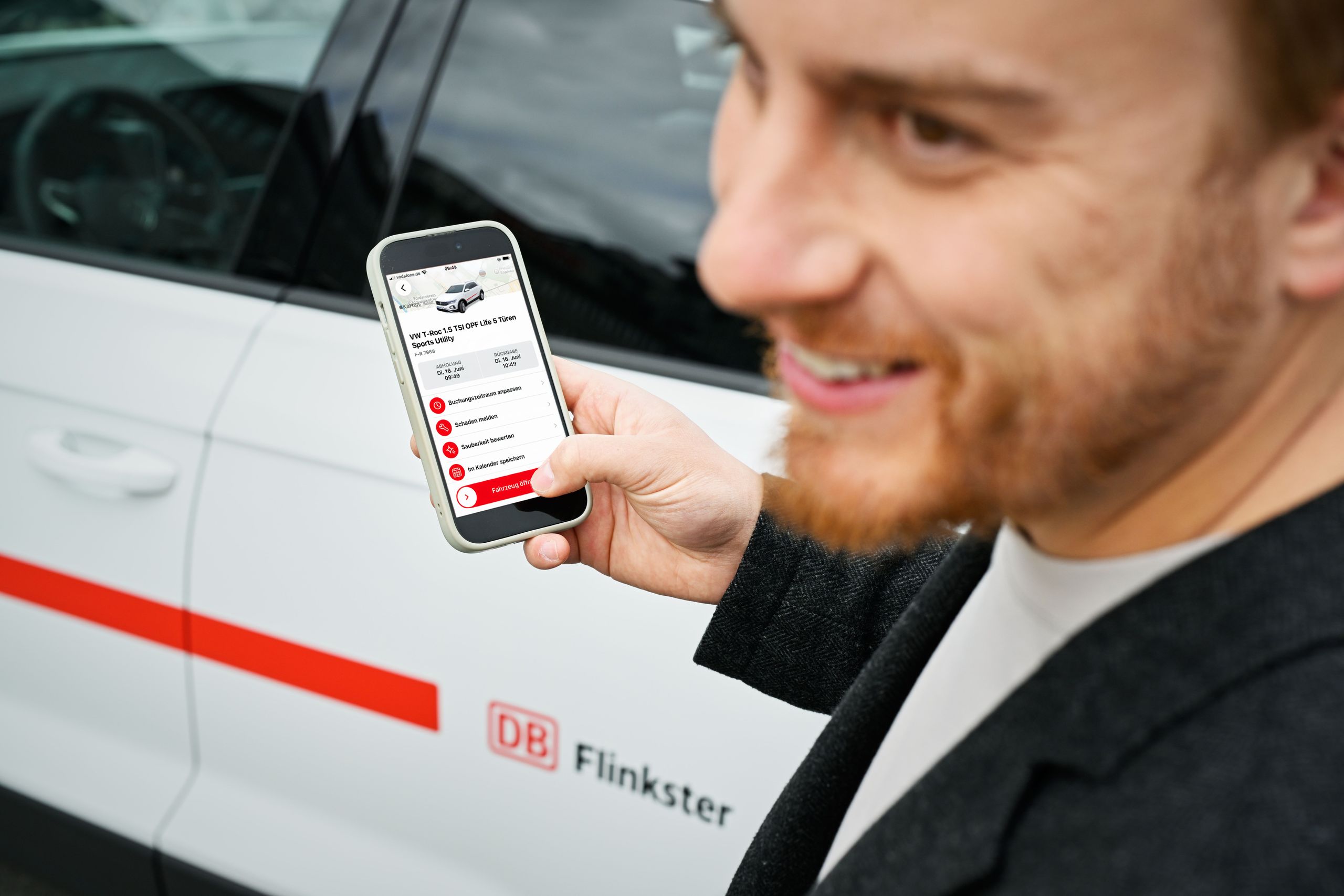 Flinkster-Kunde vor einem weißen Flinkster-Auto, schaut auf sein Smartphone, auf dem die Flinkster-App geöffnet ist.