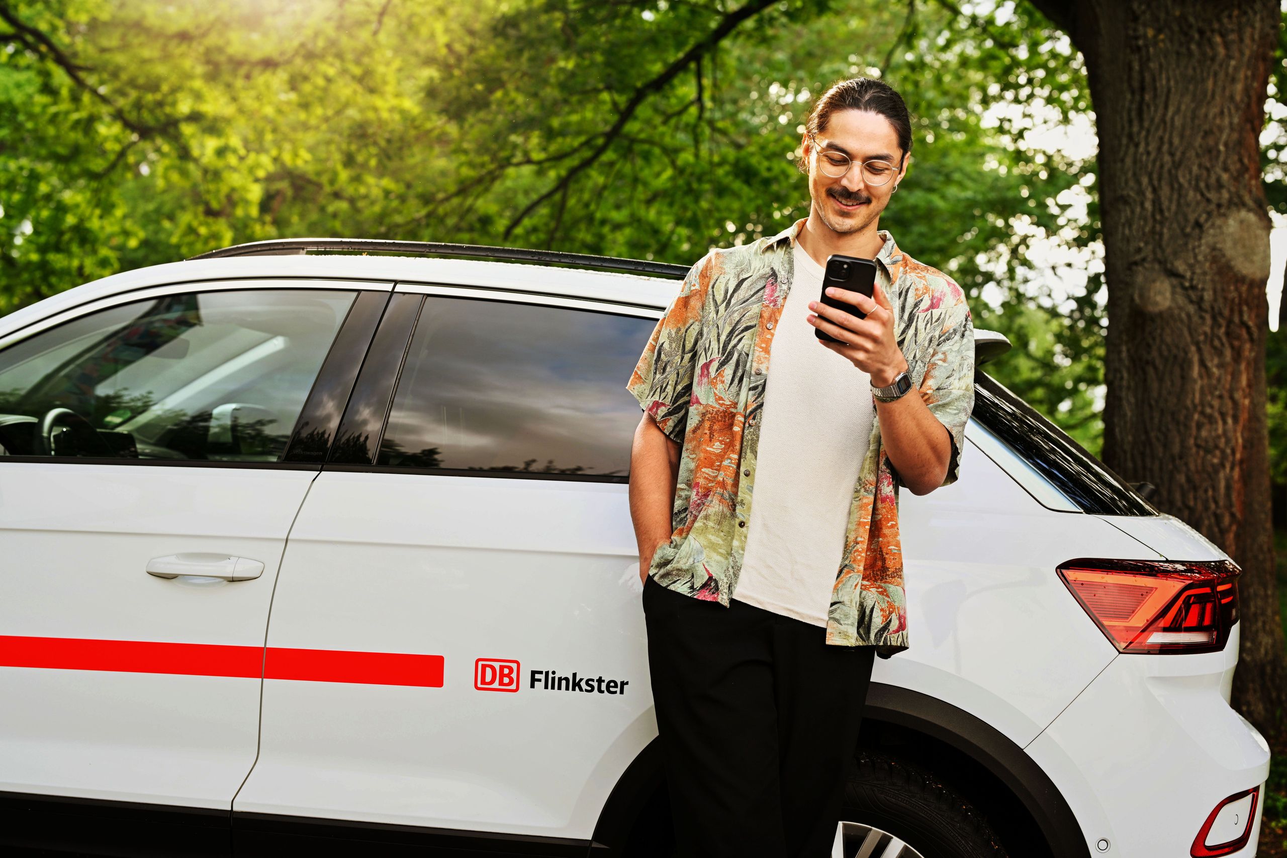 Mann lehnt entspannt am Flinkster-Auto mit Handy