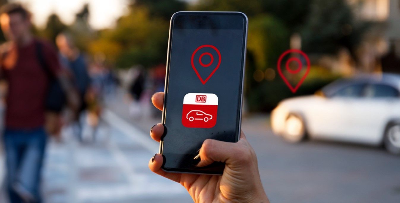 Hand hält ein Smartphone mit geöffneter Flinkster-App, im Hintergrund sind unscharf Menschen und ein Flinkster-Auto zu sehen.