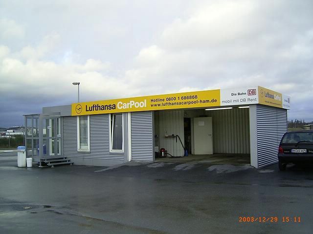 Gebäude mit einem Schild 'Lufthansa CarPool' und DB-Logo.