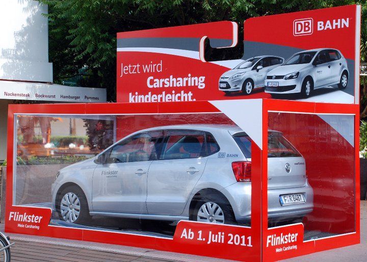 Silbernes Flinkster-Auto in einer großen Werbeverpackung mit dem Text 'Jetzt wird Carsharing kinderleicht' und 'Ab 1. Juli 2011'.