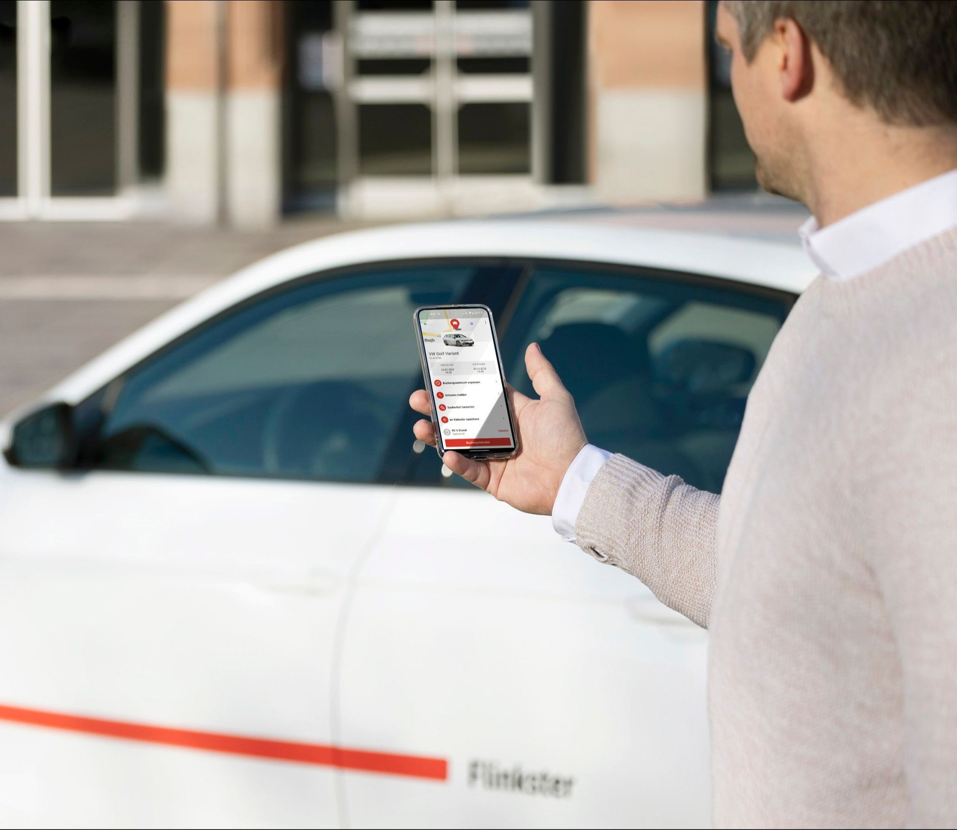 Flinkster-Kunde vor einem weißen Flinkster-Auto, schaut auf sein Smartphone, auf dem die Flinkster-App geöffnet ist.