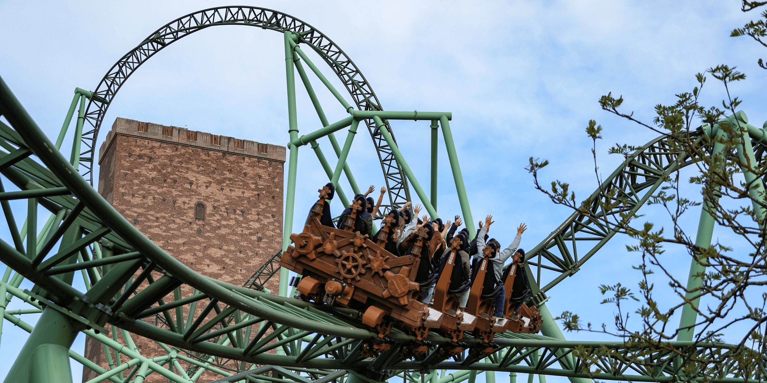 Achterbahnfahrt im Hansapark mit Passagieren, die durch grüne Stahlkonstruktionen eine Schraube fährt, vor einem gemauerten Turm. copyright Foto: istock.com/Wirestock