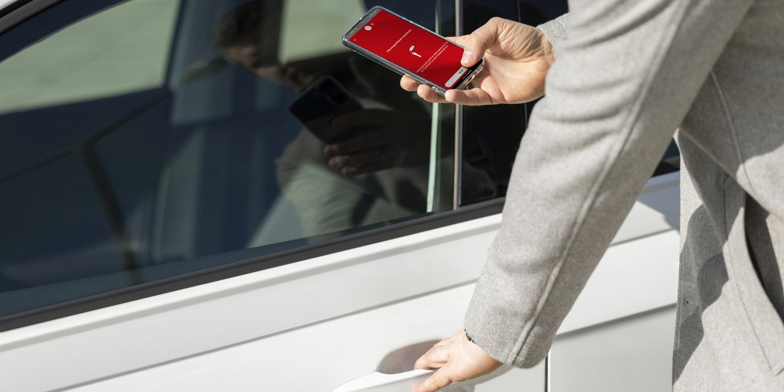 Eine Nahaufnahme zeigt eine Person, die mit ihrem Smartphone ein Flinkster-Auto entsperrt.